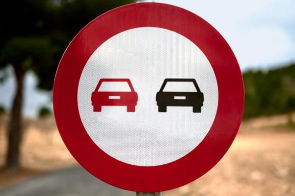 detail of a no overtaking traffic sign with a blue sky and trees in the background