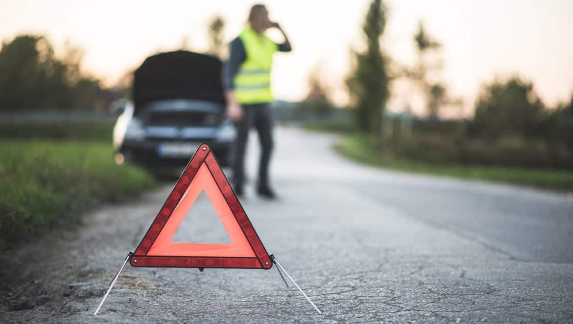 A young adult's car broke down in the middle of the road and he is using his smart phone to call for help