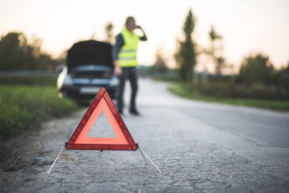 A young adult's car broke down in the middle of the road and he is using his smart phone to call for help